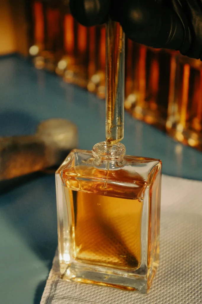 Mano di un profumiere che estrae un liquido dorato da un flacone, lavorazione artigianale del profumo